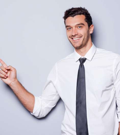 Businessman pointing copy space. Happy young man in shirt and tie looking at camera and smiling while standing against grey background and pointing copy space